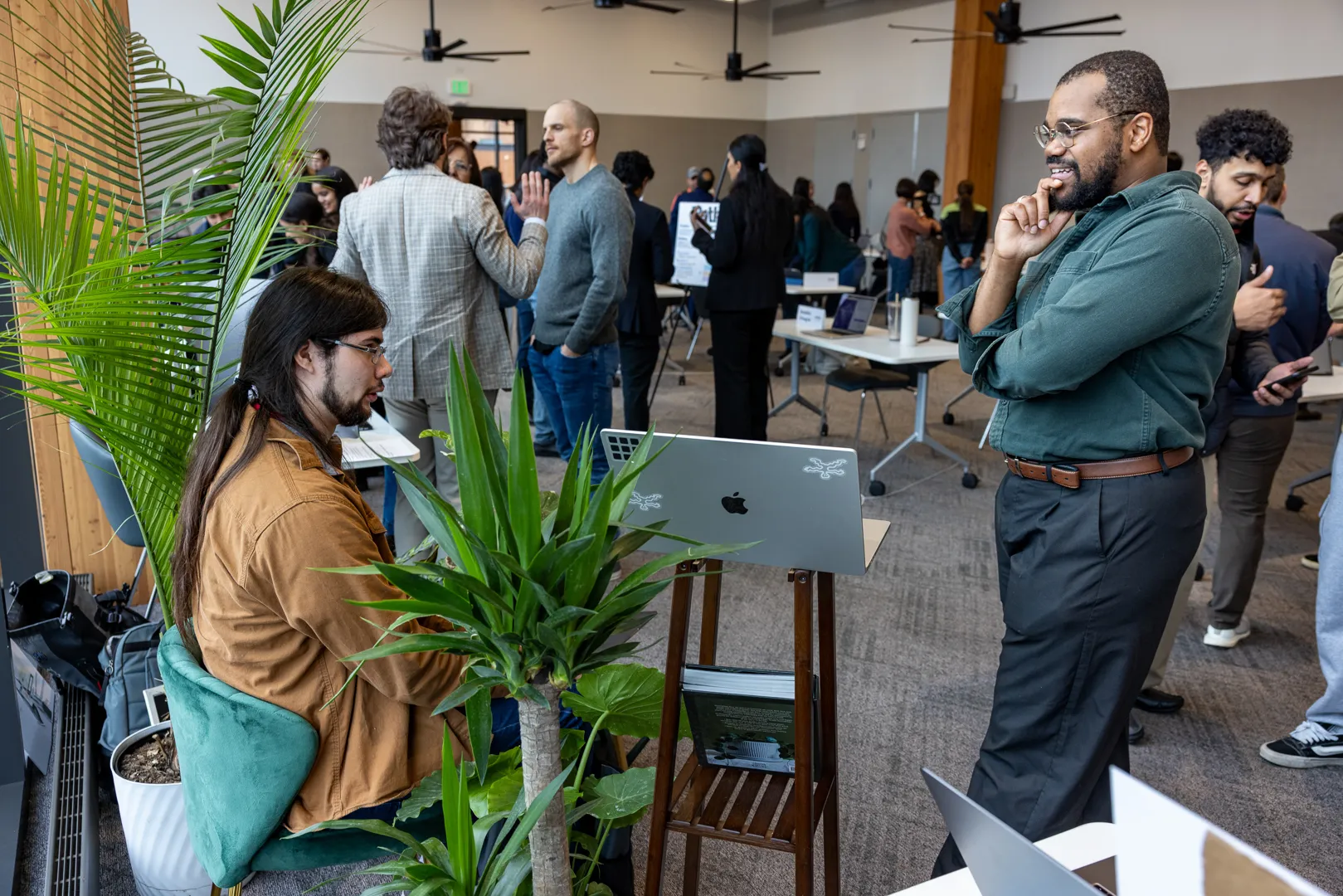 Visitors gathered around a student demo surrounded by plants in the fair space.